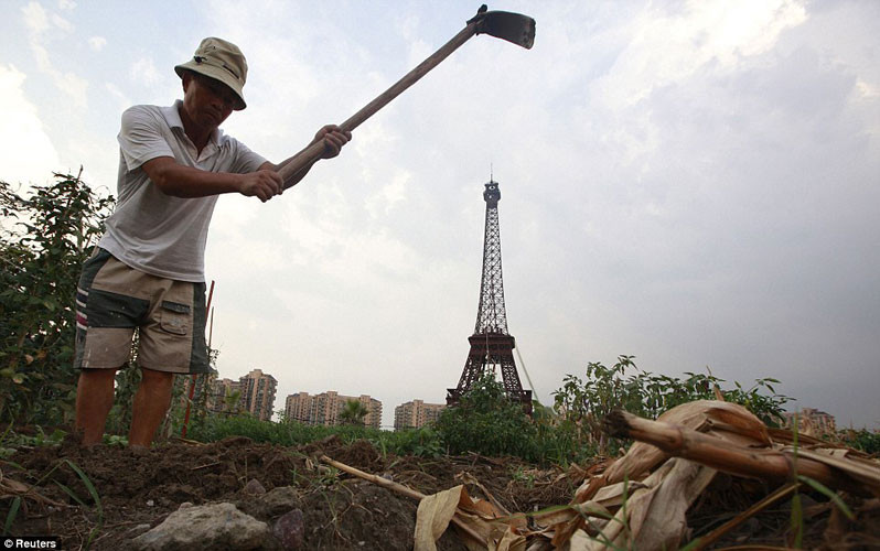 Một nông dân nghèo cần mẫn canh tác trên mảnh đất nông nghiệp mọc đầy cỏ dại ở vành đai bên ngoài Tianducheng.