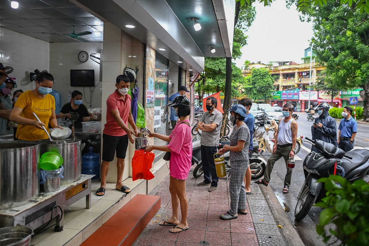 Khách tới mua phở được chủ quán yêu cầu đứng xếp hàng, đảm bảo giãn cách, nhiều người chủ động mang theo cặp lồng, hộp nhựa để giữ phở nóng và đảm bảo vệ sinh.