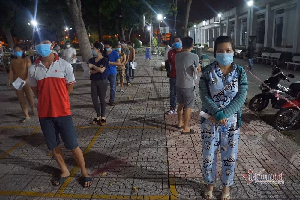 Theo ghi nhận, từ 19h tối, người dân từ các khu phố bắt đầu đổ về điểm tiêm trường THPT Trường Chinh để làm thủ tục vào bên trong. Mặc dù số lượng đông nhưng mọi người đều tuân thủ quy định phòng dịch, xếp hàng trật tự.