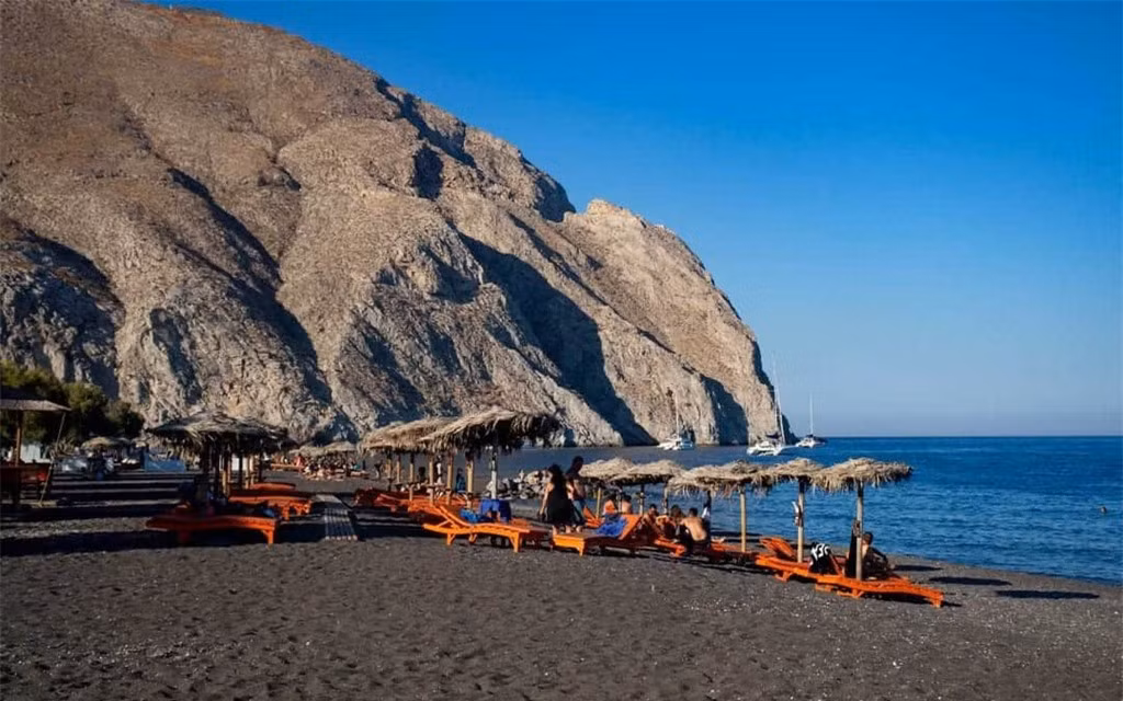 Bãi biển Perissa (Hy Lạp):Nằm dọc bờ biển phía Nam Santorini, địa điểm thu hút rất nhiều người ghé đến check-in bởi vẻ đẹp của những bãi cát màu đen huyền bí. Màu sắc cát được tạo thành từ nham thạch phun trào của núi lửa Minoa qua thời gian. Để tận hưởng kỳ nghỉ hoàn hảo, du khách chỉ cần thư giãn trên những chiếc ghế dài, thưởng thức ly cocktail dưới chiếc ô làm bằng lá cọ. Ảnh:Delve Into Europe.