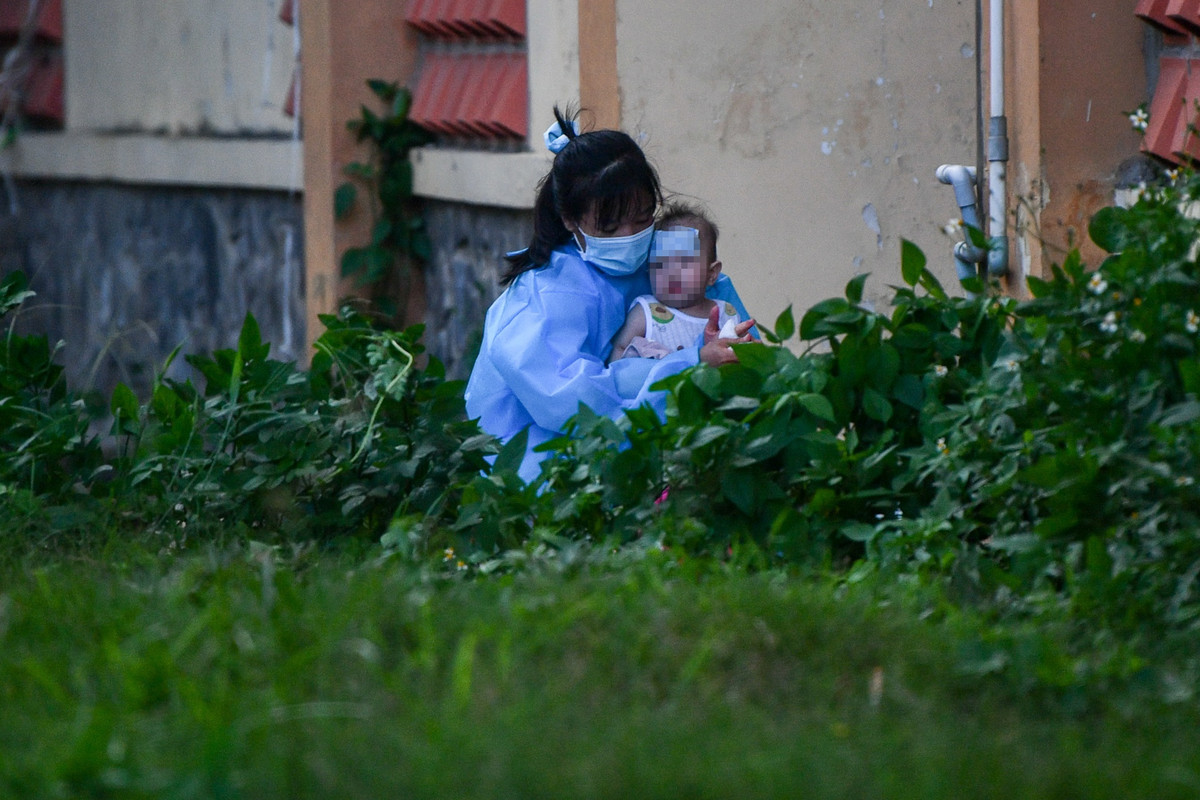 Trong khuôn viên bệnh viện, một bệnh nhi có biểu hiện sốt cao được mẹ chuẩn bị đồ đạc trước khi xe cấp cứu đến chuyển đi.