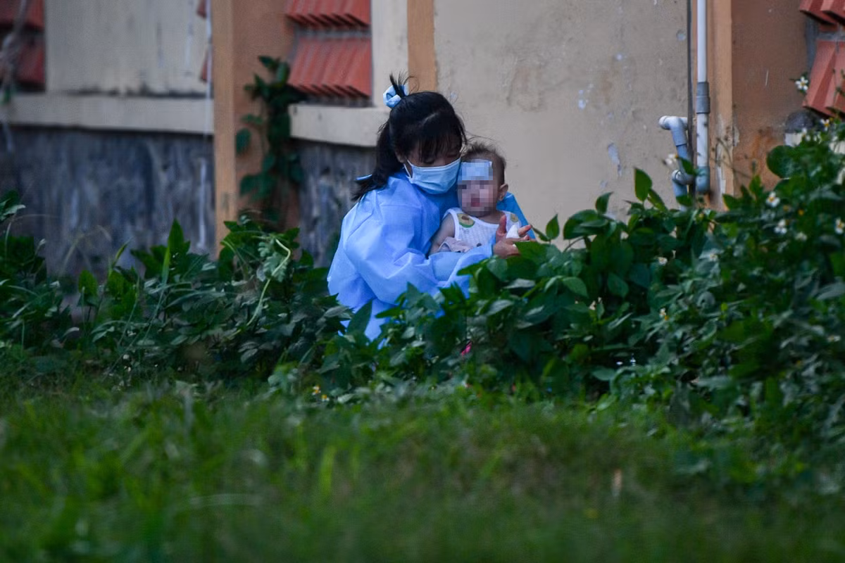 Trong khuôn viên bệnh viện, một bệnh nhi có biểu hiện sốt cao được mẹ chuẩn bị đồ đạc trước khi xe cấp cứu đến chuyển đi.