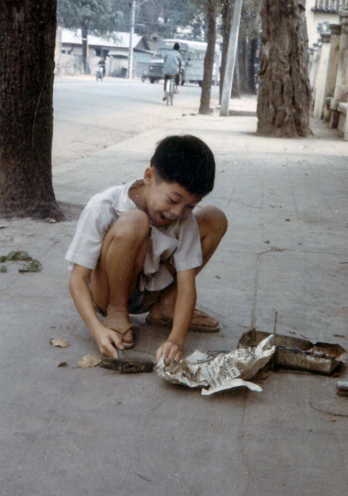 Cậu bé nghịch búa và đinh trên vỉa hè.