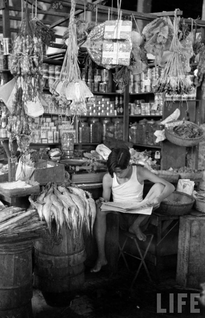 Nam thiếu niên đọc báo khi trông quầy hàng đồ khô ở chợ.