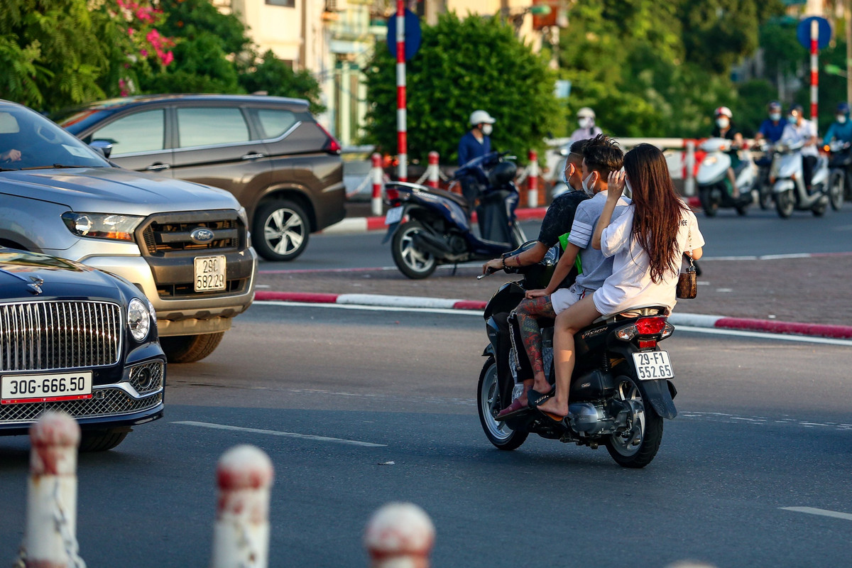 Một chiếc xe máy chở 3 người không đội mũ bảo hiểm bất chấp nguy hiểm đi lách qua nhiều ôtô để sang làn đường bên kia.