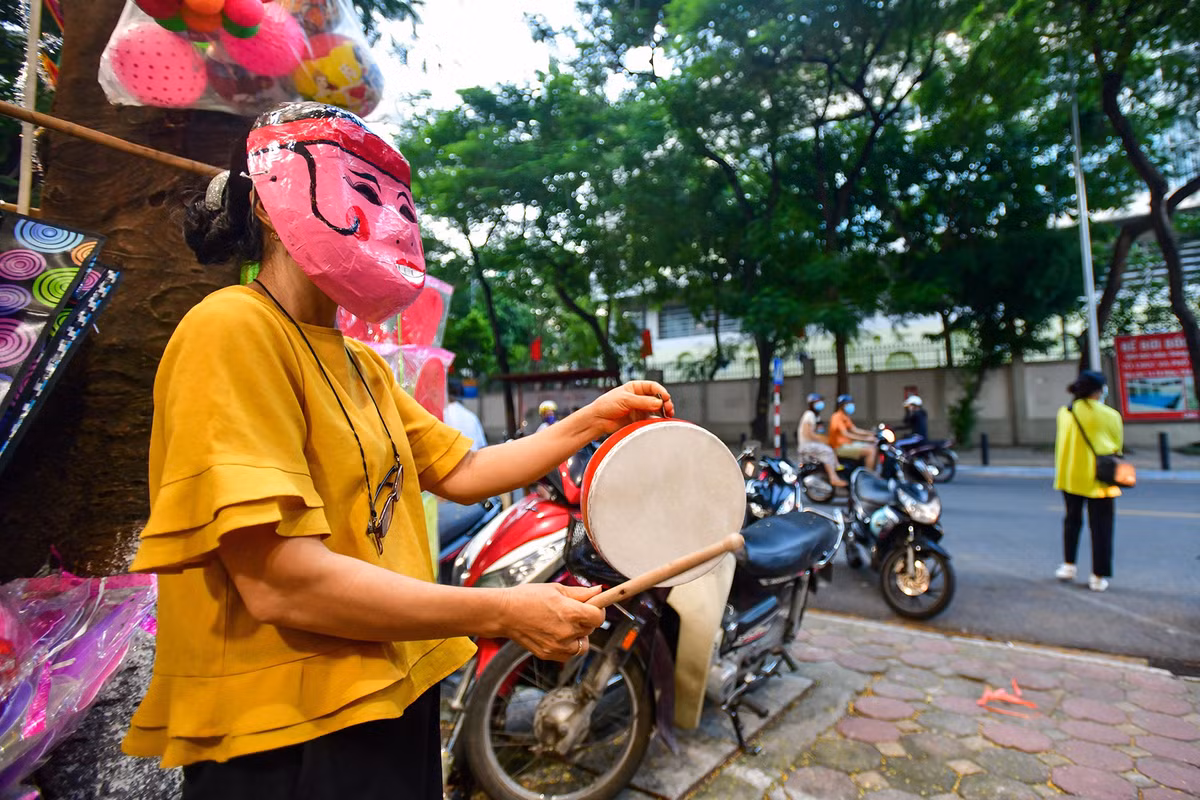 Chị Đặng Thị Lược (53 tuổi), chủ một cửa hàng văn phòng phẩm, hóa trang thành ông địa gõ trống để gây sự chú ý với khách hàng. Hình ảnh này vốn xuất hiện ở chợ Trung thu phố cổ Hàng Mã, Hàng Lược những năm trước khi chưa có đại dịch.