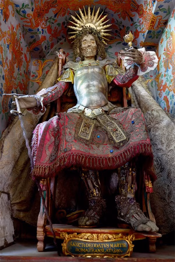 Bộ xương của Thánh Deodatus. Một trong những khám phá thú vị nhất củaPaul Koudounaris chính là bộ xương St. Deodatus được tìm thấy ở Moosburg, Đức, bộ xương nàyvẫn còn nguyên những viên ngọc được gắn trên đó. Ông từngkhông thể giấu được niềm vui sướng: "Nhà thờ cho phép tôi lấy bộ xương ra khỏi hộp, thật sự đó là một cảm giác khó tả, dường như có một sợi dây gắn kết và duyên số đã để tôi được gặp di vậtsau 2 thế kỷ.”Vẫn còn nhiều bí ẩn về những bộ xương nạm ngọc ngà này, nhiều người rất muốn được chiêm ngưỡng chúng.Các bộ xương vô giá này được xem là biểu tưởng sức mạnh mới được tìm thấy của Giáo hội Công giáo ở những khu vực trước đây thuộc đạo Tin lành.