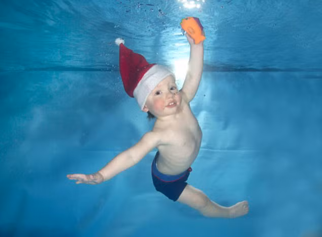 Em bé đội mũ Noel đùa nghịch dưới nước.