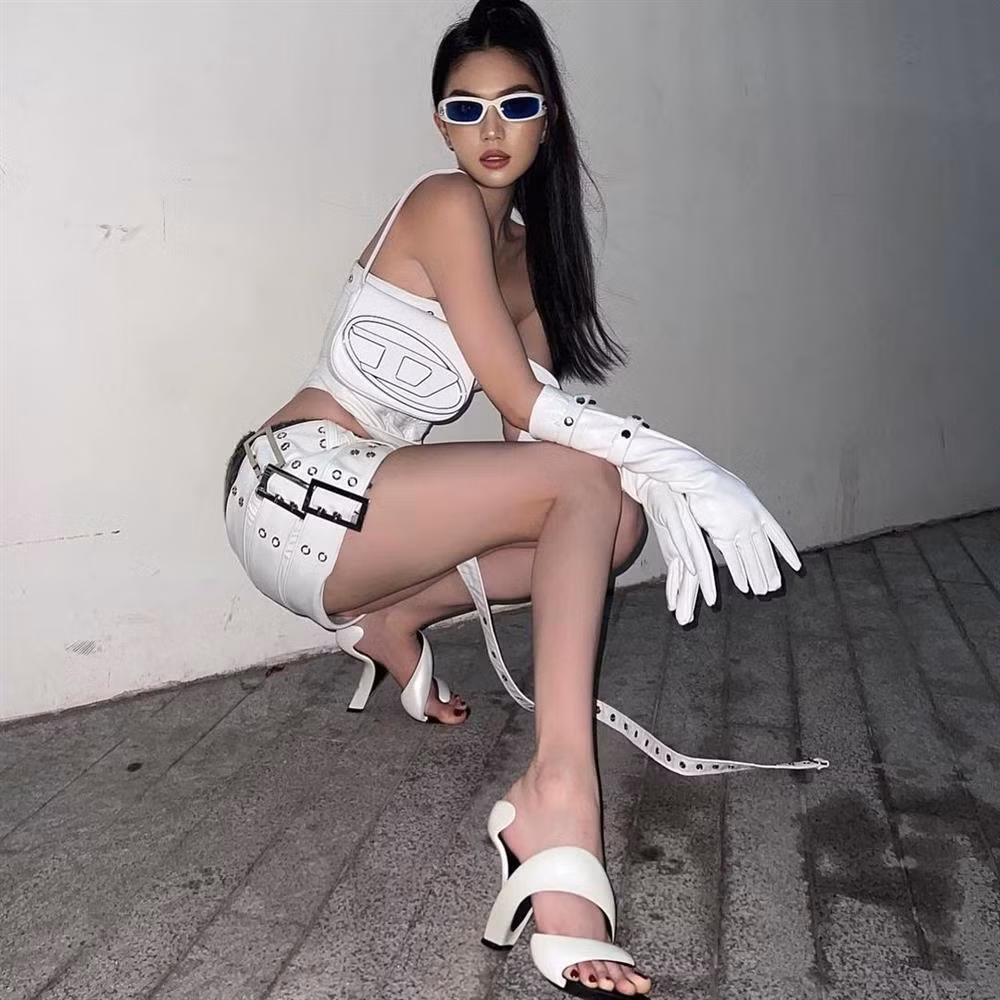 Điểm khác biệt dễ nhận thấy là Ngọc Trinh chỉ buộc đuôi ngựa thay vì thắt bím, đeo thêm găng tay, túi xách Diesel và chọn một đôi sandal lạ mắt đến từ Julian Hakes.