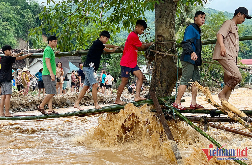 Nhiều cơ quan hành chính cấp huyện, nhà dân, ki-ốt bị cây cối, đất đá luồn vào và vây quanh khiến việc tiếp cận và cứu vớt tài sản ở phía trong gặp nhiều khó khăn. (Người dân đi qua cây cầu tạm vừa làm xong sáng 3/10 ở xã Tà Cạ - Ảnh: Quốc Huy) 