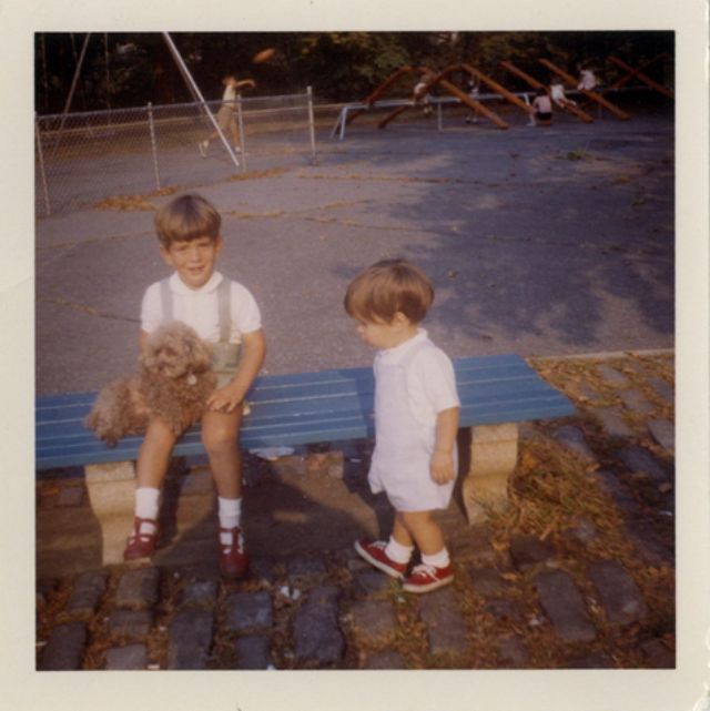 Cậu bé John F. Kennedy Jr. ôm chú chó nhỏ khi ngồi trên băng ghế.