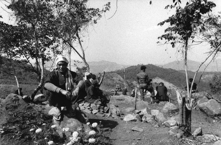 Nhóm trại viên trại Doi Tong nghỉ ngơi trong một buổi lao động ngoài trời. Một quân nhân cầm súng máy đứng canh nhóm người này. Ảnh: Patrick Zachmann/ Magnum.