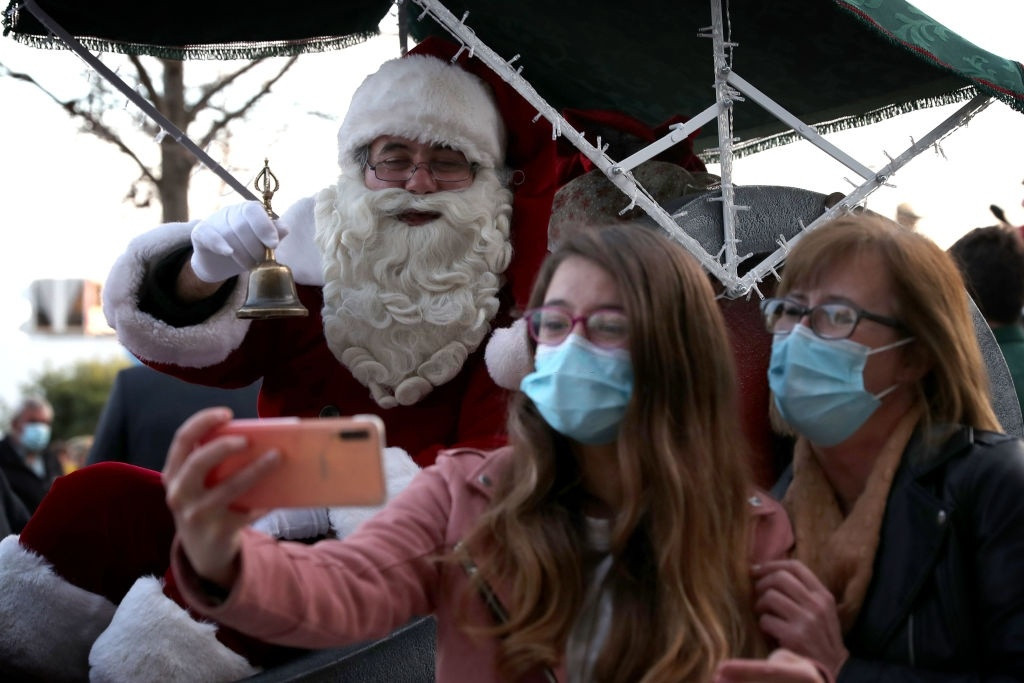 Ông già Noel chụp ảnh cùng hai vị khách nữ đeo khẩu trang. Ở nhiều nơi trên thế giới, các ông già Noel còn không được chụp hình cùng khách để đảm bảo yêu cầu giãn cách. Ảnh: Pedro Fiúza. corona_counter.css