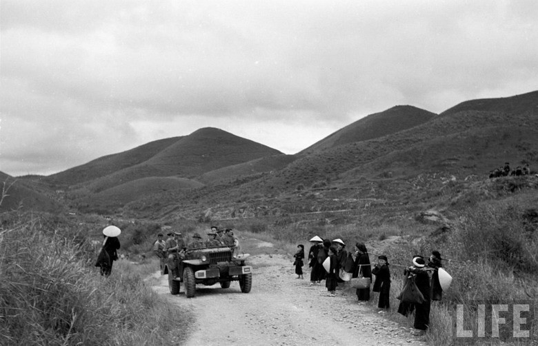 Người dân địa phương tò mò đứng nhìn khi một chiếc xe chở lính Pháp chạy qua.