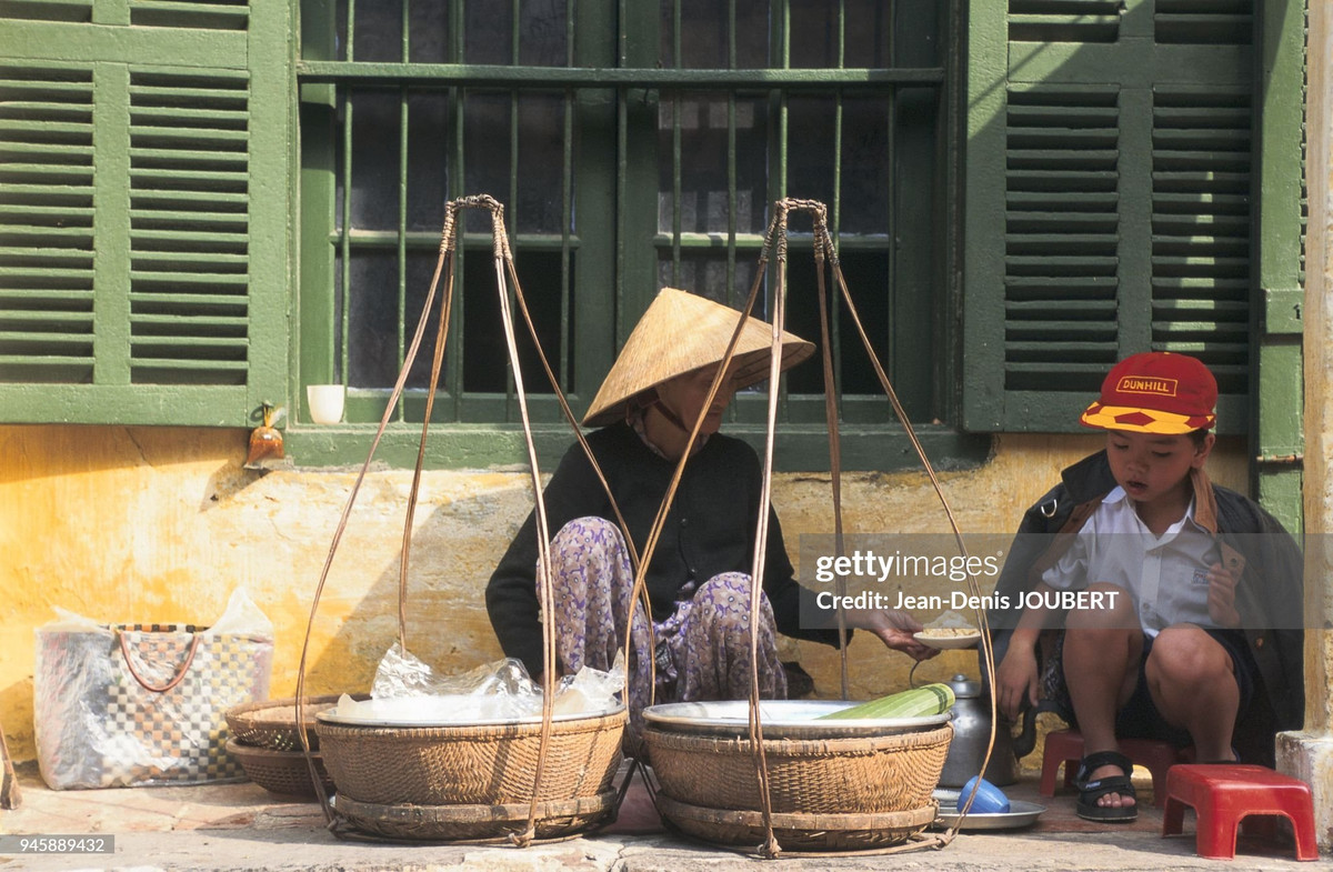 Cậu bé ăn sáng ở gánh hàng rong của bà cụ.