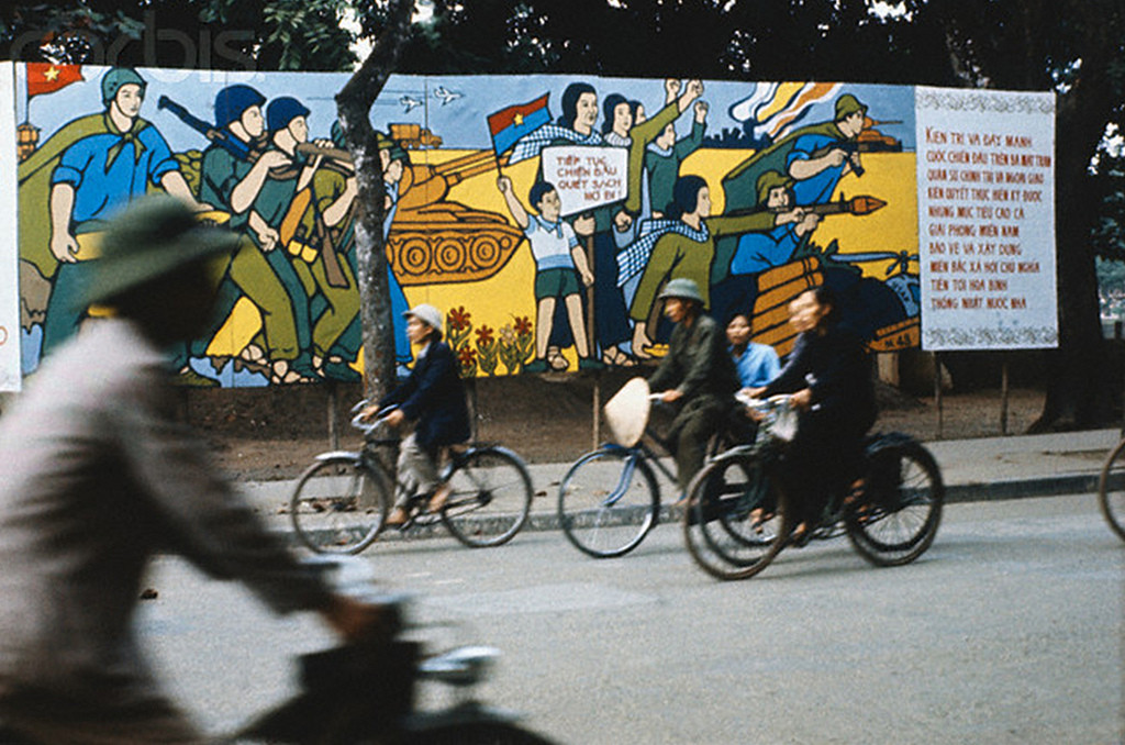 Người dân đạp xe qua bức tranh cổ động kháng chiến chống Mỹ trên đường phố.