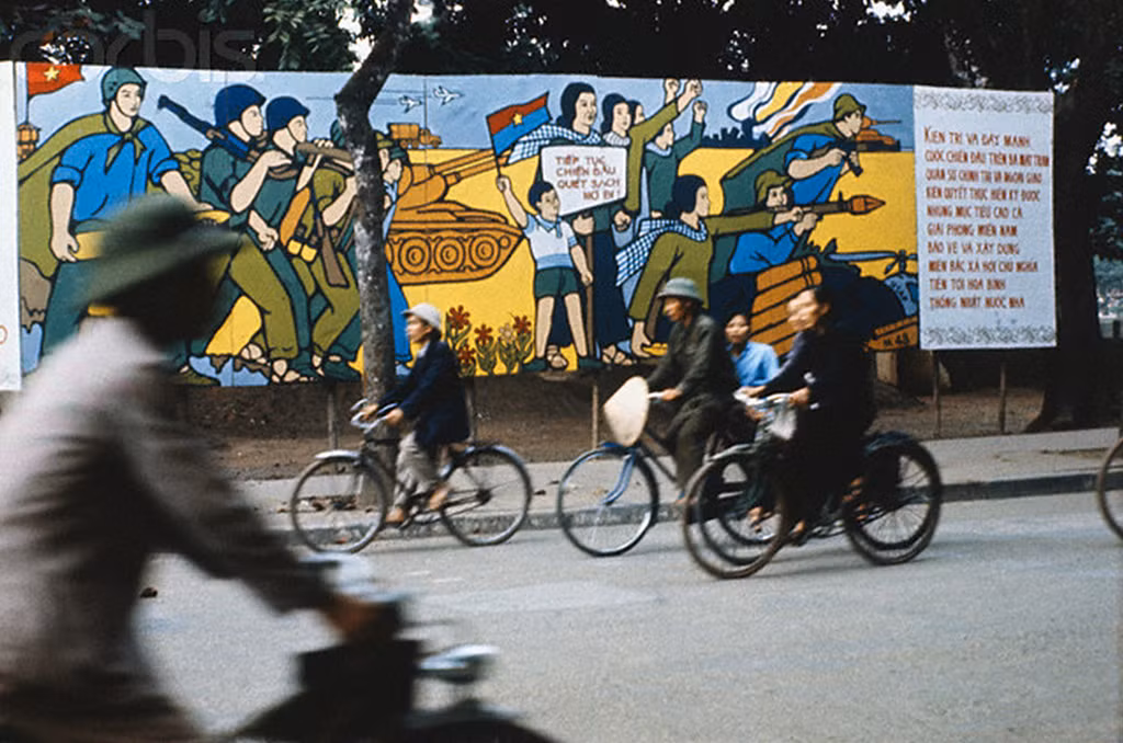 Người dân đạp xe qua bức tranh cổ động kháng chiến chống Mỹ trên đường phố.