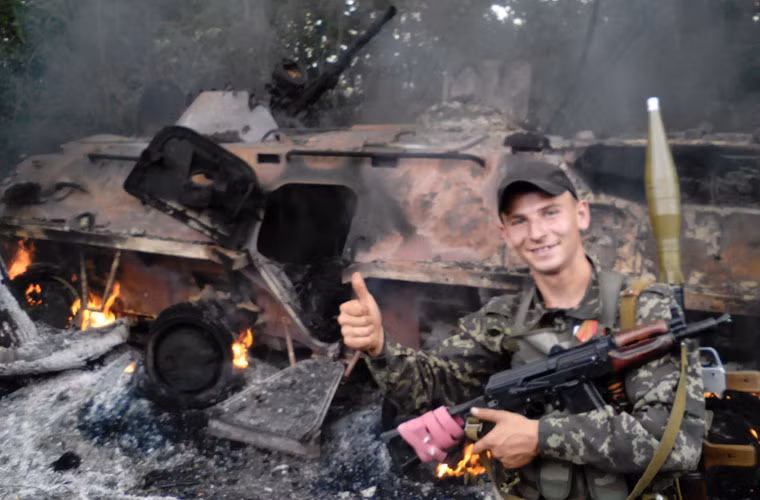 Tay súng quân ly khai đứng trước xác xe thiết giáp chở quân BTR-80 của Quân đội Ukraine bị phá tan tành, ngày 18/6/2014.
