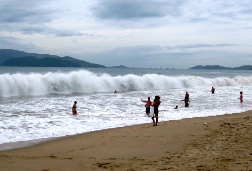 Phía trước sóng đang cuồn cuộn. Nhiều du khách tranh thủ chụp hình với sóng lớn. Do bão đang về nên nước biển hôm nay trắng đục, không trong xanh như mọi hôm.