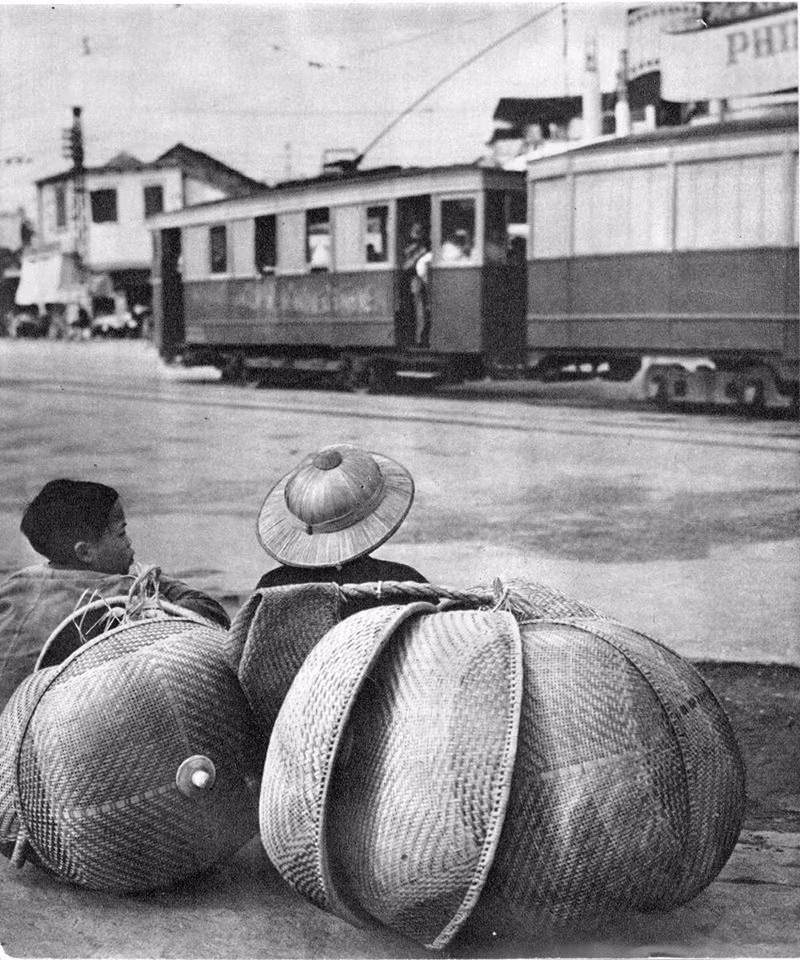 Hai em bé bán lồng bàn gần bến tàu điện bờ hồ Hoàn Kiếm, thập niên 1950. Trong Toàn quốc kháng chiến tháng 12/1946, các toa tàu điện đã được những người lính vệ quốc biến thành chướng ngại vật rất hiệu quả nhằm ngăn chặn bước tiến các đoàn xe cơ giới của thực dân Pháp trên đường phố Hà Nội. Ảnh: Rév Miklós.