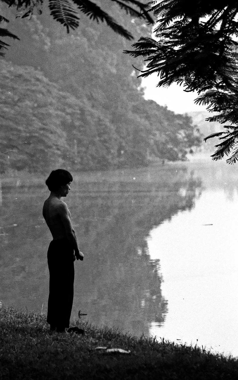 Một nam giới tập khí công bên bờ hồ buổi sáng sớm.