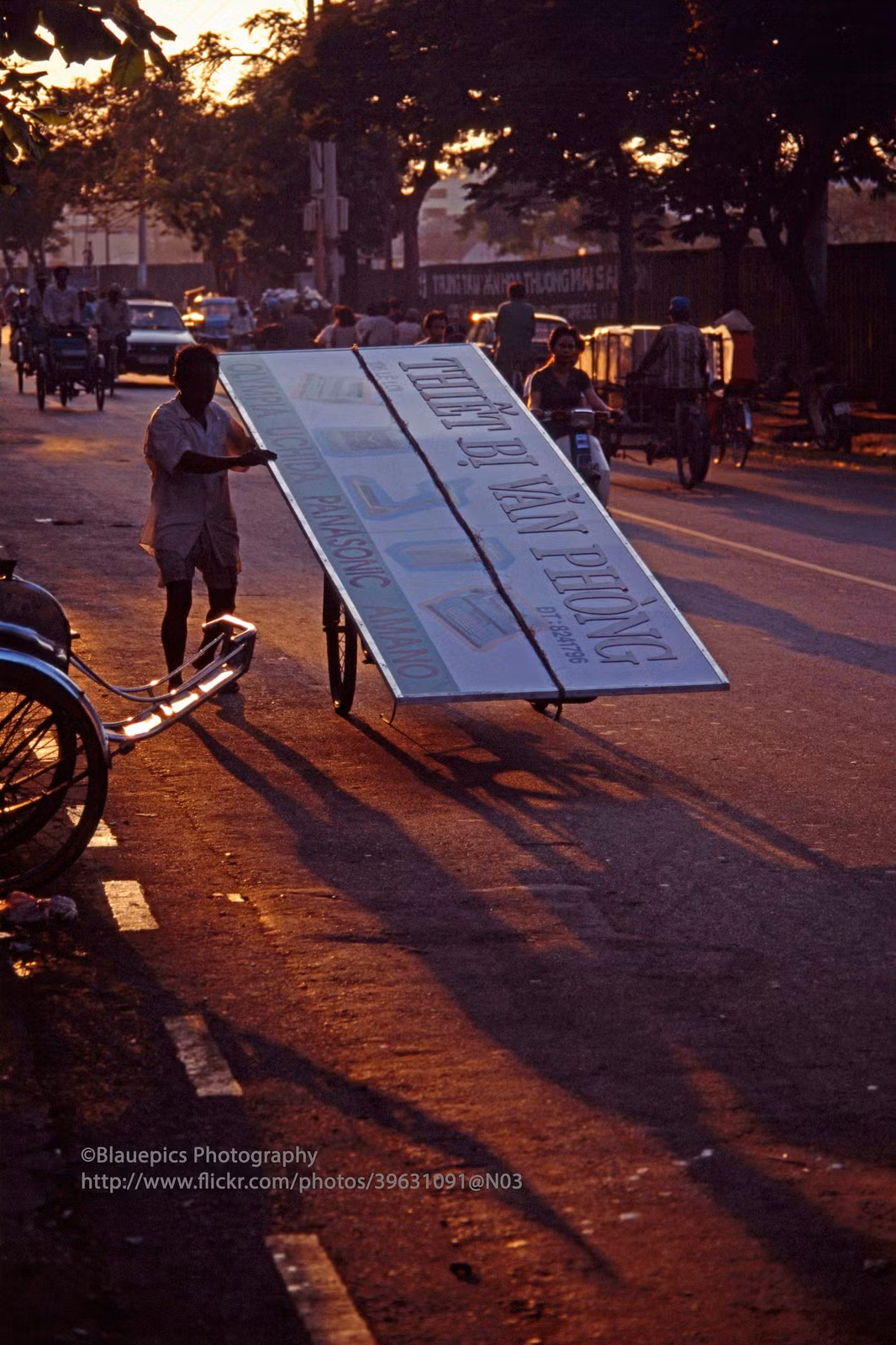 Người lái xích lô vận chuyển tấm bảng hiệu cỡ lớn trên chiếc xích lô của mình.