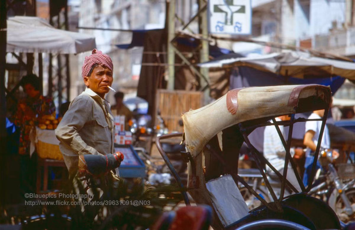 Người lái xích lô đứng bên đường.