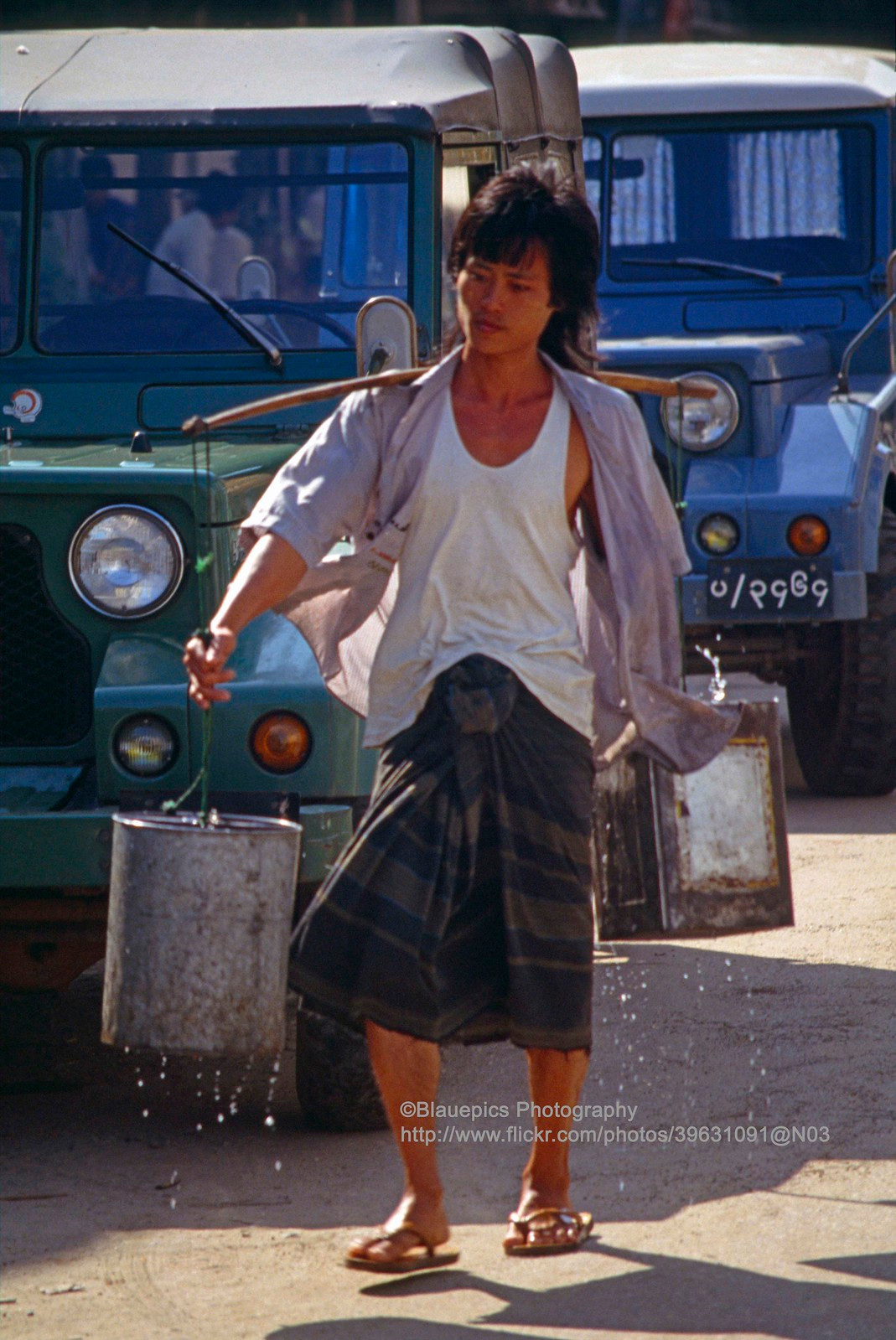 Nam thanh niên mặc sarong gánh nước trên phố.