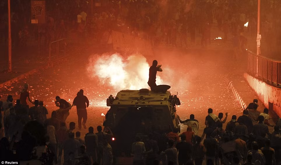Đám đông người biểu tình phản đối cựu Tổng thống bị lật đổ Morsi tập trung sau chiếc xe bọc thép chở cảnh sát chống bạo động Ai Cập (bắn đạn cao su về phía các thành viên Anh em Hồi giáo và người ủng hộ ông MorsiL.