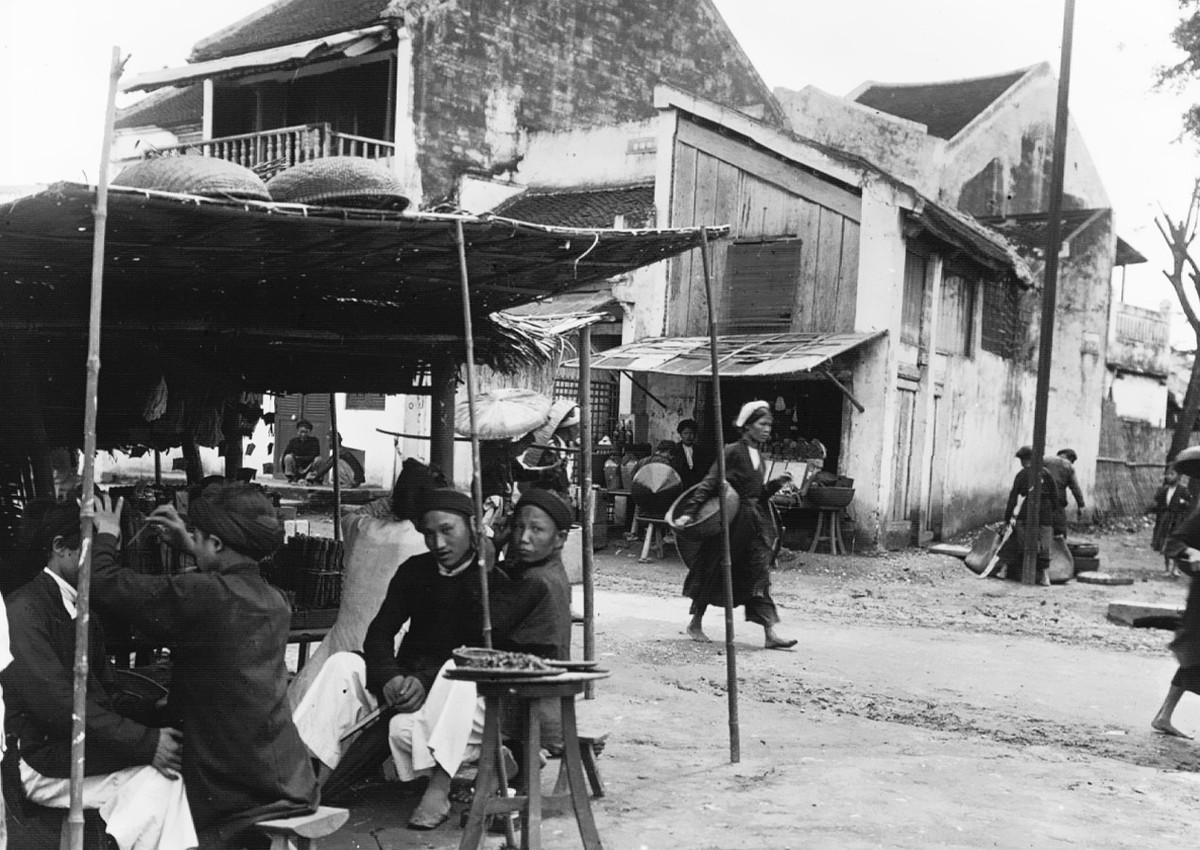 Cảnh hớt tóc, lấy ráy tai ở một quán cóc vỉa hè Hà Nội năm 1896. Việc lấy ráy tai được người thợ thực hiện rất khéo léo với một que kim loạt nhỏ uốn cong. Ảnh: Firmin-André Salles.