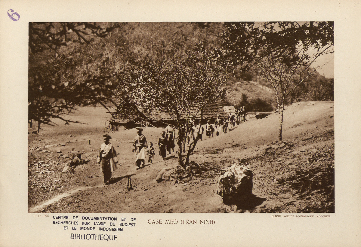 Các phụ nữ và trẻ em của nhiều gia đình người H'Mông đi lễ tại một bản ở Lào, thuộc vùng Trấn Ninh cũ. Nhà của họ được dựng trên nền đất, lợp bằng ngói gỗ. Xung quanh nhà trồng một số cây ăn quả, cụ thể là cây đào.