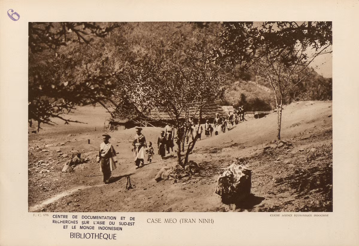 Các phụ nữ và trẻ em của nhiều gia đình người H'Mông đi lễ tại một bản ở Lào, thuộc vùng Trấn Ninh cũ. Nhà của họ được dựng trên nền đất, lợp bằng ngói gỗ. Xung quanh nhà trồng một số cây ăn quả, cụ thể là cây đào.