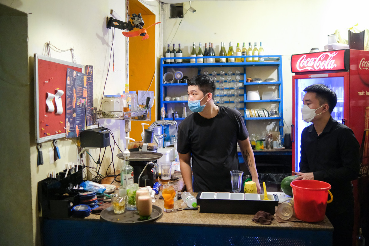 Trong quầy pha chế, Đạt (bên phải) cũng tất bật, liên tục hoạt động không ngơi tay. "Bình thường, mình có thêm một đồng đội nữa, hai người hỗ trợ lẫn nhau. Nay chỉ mình đứng quầy nên phần việc tăng lên gấp đôi", Đạt chia sẻ. Lâu ngày mới động vào cốc chén, dụng cụ pha chế quen thuộc, anh cảm thấy "hơi bị ngợp", "chưa quen tay hẳn".