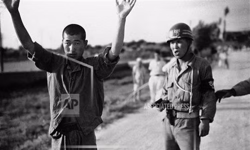 Cảnh sát quân sự Hàn Quốc dẫn giải tù binh Triều Tiên với khẩu súng ngắn trong tay. Ảnh chụp ngày 21/7/1950.