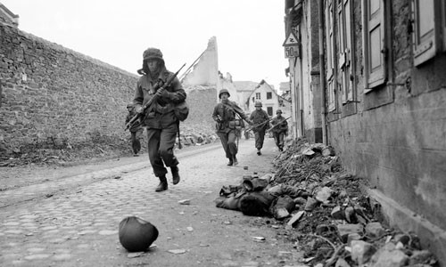 Binh sĩ Mỹ vội vã di chuyển ở Coblenz, Đức ngày 18/3/1945. Thi thể một binh sĩ tử trận nằm bên vệ đường.