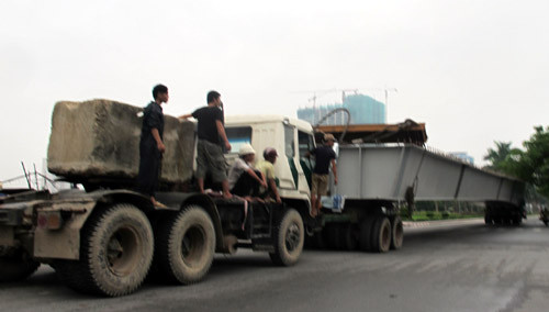 Một xe kéo, một xe đẩy chạy trên đường, công nhân đu bám bên khối bê tông lớn.