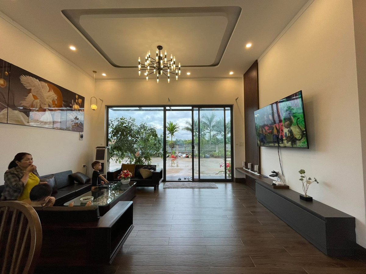 Nhà có nền khá cao, phía trước bậc tam cấp làm rộng để các cháu có chỗ ngồi chơi, hóng gió. Hai bên là cây cảnh, hoa rực rỡ quanh năm. Khung cửa kính lớn giúp người lớn ở trong nhà vẫn để ý được trẻ con đang chơi bên ngoài.