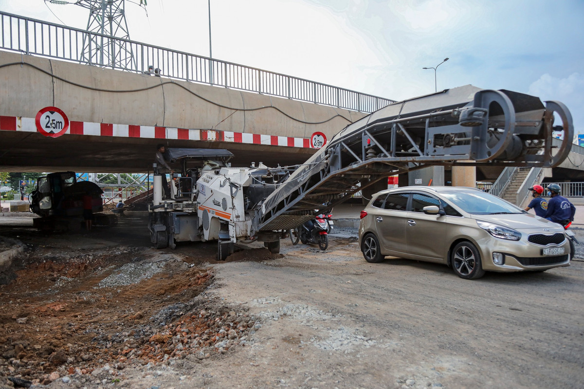 Bên dưới dạ cầu Bưng, các thiết bị chuyên dụng của nhà thầu đang cào bóc lớp đường cũ, sau đó thay thế bằng lớp nhựa mới để đảm bảo cao độ thông xe.