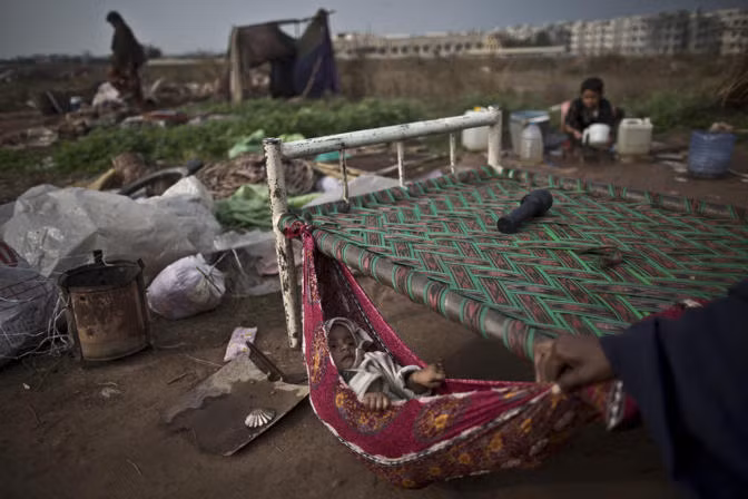 Một em bé say ngủ trên chiếc võng mắc tạm vào đầu một chiếc giường đặt ở ngoài trời sau khi ngôi nhà dột nát của gia đình bé bị phá dỡ. Tai họa này biến cả gia đình bé trở thành những người vô gia cư.