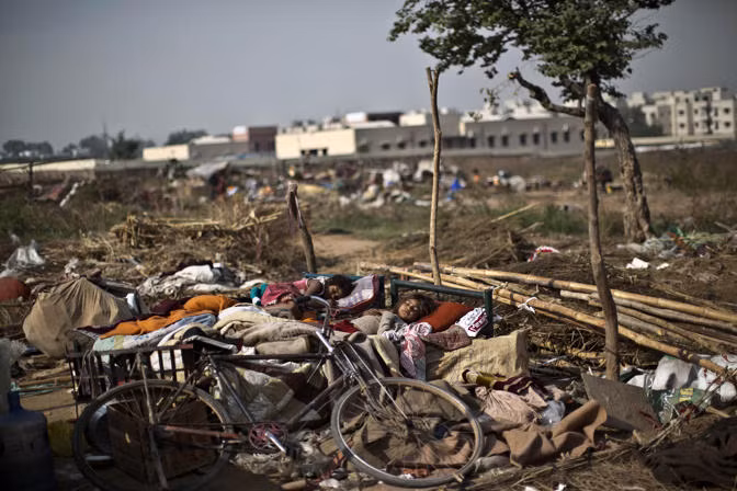 2 chị em gái ngủ trên chiếc giường được kê ngoài trời bên cạnh đống đồ đạc lộn xộn sau khi mất nhà.