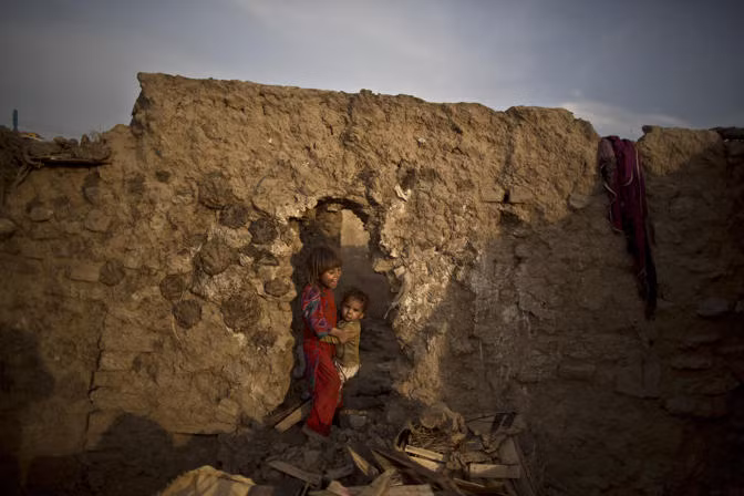 Một bé gái Pakistan sống ở khu ổ chuột bên ngoài ngoại ô Islamabad cố gắng bồng em trai nhỏ đi qua một lỗ hổng - lối ra vào ngôi nhà của 2 chị em.