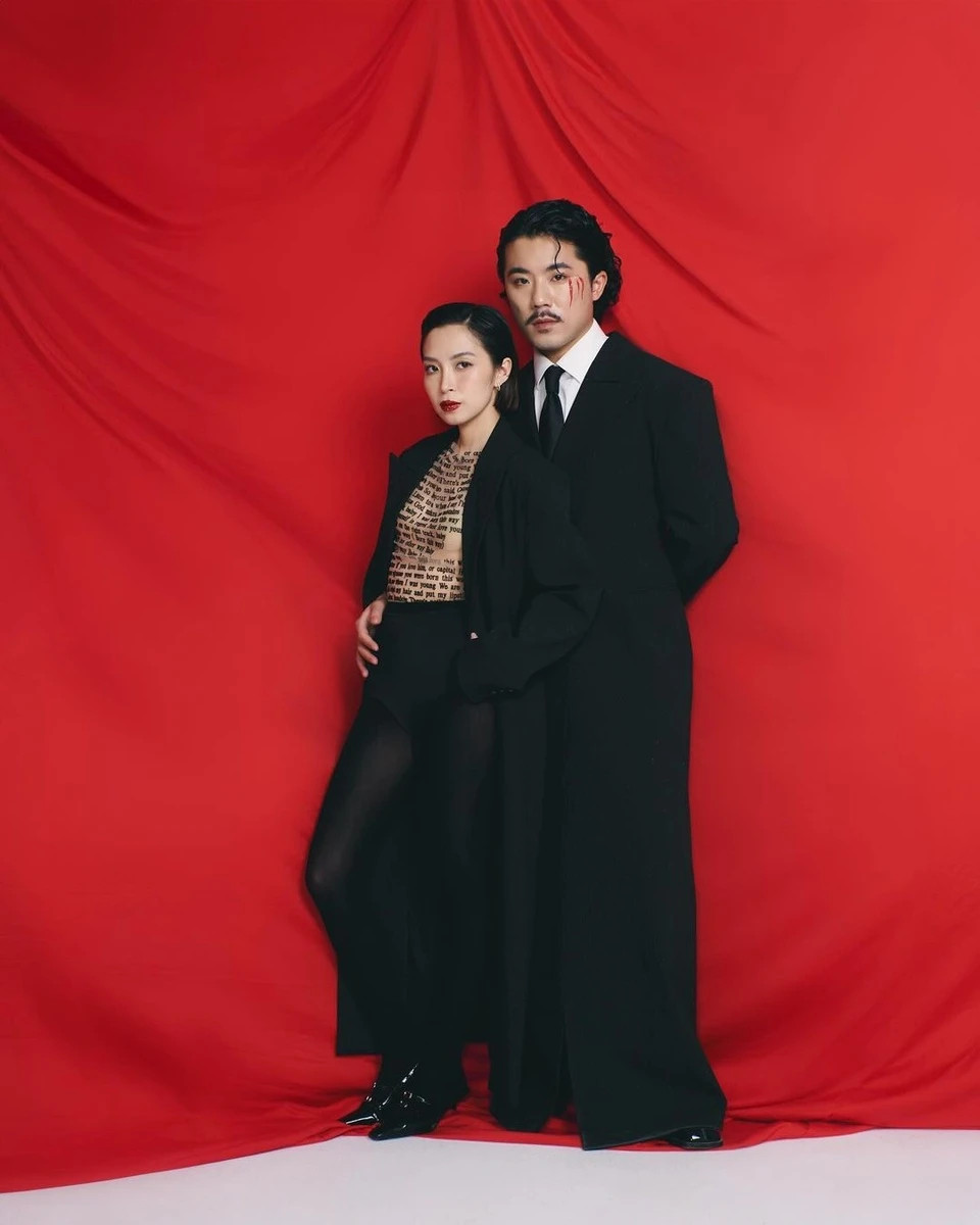 Vợ chồng Đức Triệu - Linh Bùi tôn vinh tính nữ qua set trang phục ton-sur-ton. Cả 2 cùng diện áo dạ dáng dài màu đen, theo đuổi xu hướng gender-fluid (linh hoạt giới). Đức Triệu chọn sơ mi trắng, caravat đen, quần lửng và vớ da chân chấm bi. Anh làm nền cho bà xã trong bộ hình này. Linh Bùi phối áo không tay trong suốt với quần lót cạp cao màu đen và vớ đồng màu. Cô nhiệt tình hưởng ứng mốt không quần được nhiều ngôi sao, tín đồ thời trang lăng xê. Cách kết hợp nội y tam giác và vớ da chân cũng từng được các minh tinh như Kylie Jenner hay Kendall Jenner ứng dụng thành công. Ảnh: @lovvin.family.