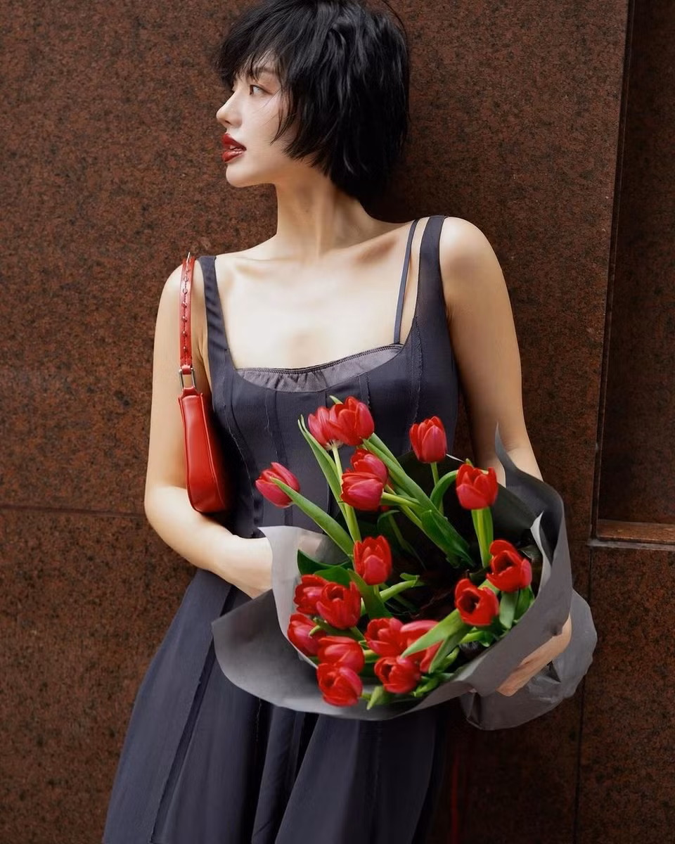 Khánh Linh (Cô Em Trendy) cũng không bỏ qua ngày lễ đặc biệt này. Không hoá thân thành bông hoa như Quỳnh Anh Shyn, cô coi bó tulip đỏ là món phụ kiện, tạo dấu ấn cho set trang phục nữ tính, cổ điển. Khánh Linh mặc váy 2 dây bổ sung đường gân tôn dáng của thương hiệu Mango. Mặc đầm đen tối giản, thanh lịch, cô thể hiện khả năng “chơi” phụ kiện ấn tượng. Túi xách, giày cao gói, son và bó hoa trên tay Khánh Linh đều có màu đỏ. Đây cũng là màu sắc được nhiều ngôi sao, nhà mốt lăng xê trong mùa thời trang đầu năm nay. Ảnh: @klinhnd.