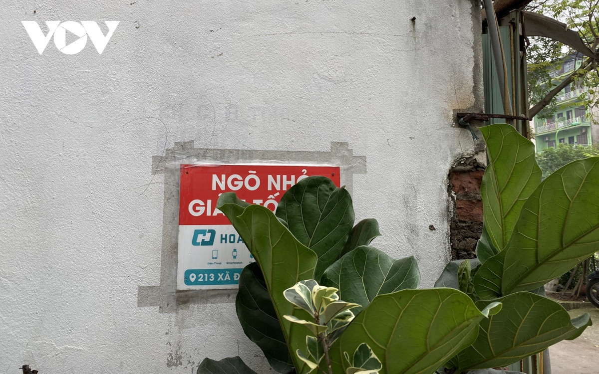 Một biển báo nhỏ "Ngõ nhỏ, giảm tốc độ" được dán lên tường nhà, nhưng bị cây xanh che khuất.