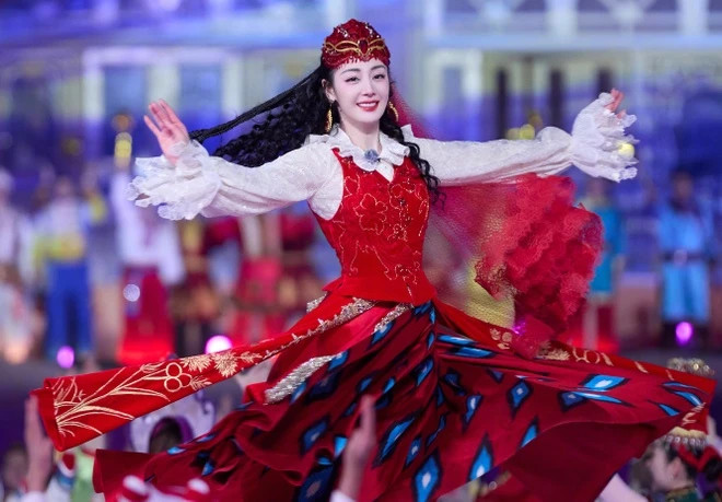 Theo Sina, Kashgar là địa khu thuộc Khu tự trị dân tộc Uyghur Tân Cương, Trung Quốc. Địch Lệ Nhiệt Ba 15 tuổi đã trở thành diễn viên múa tại Đoàn ca múa Tân Cương. Trong chương trình Xuân Vãn, nữ diễn viên cùng với đồng bào đã thể hiện tiết mục Vũ nhạc Tân Cương quyến rũ, vui nhộn. Thời tiết tại Kashgar là -2 độ C nhưng Nhiệt Ba vẫn thể hiện sự tươi tắn, tự hào.