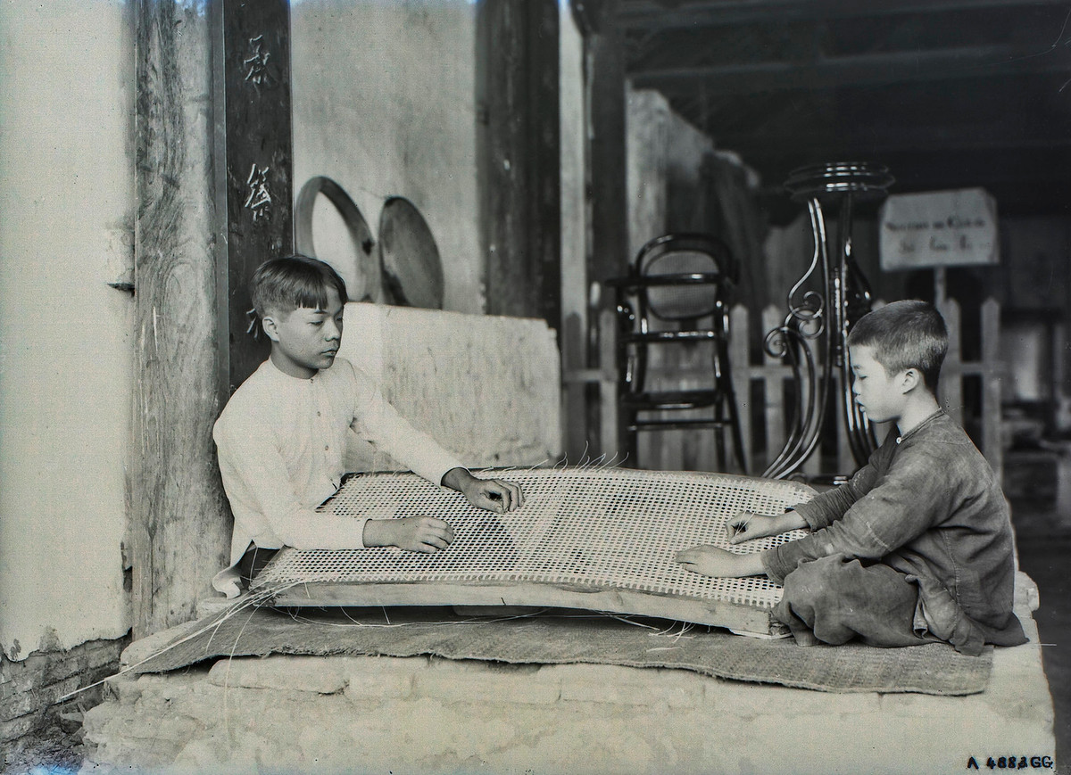 Hai cậu bé đan lạt tre tại một cơ sở sản xuất bàn ghế mây.