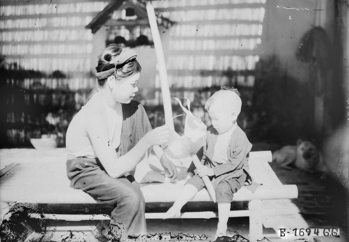 Người phụ nữ ngồi trên chõng tre cùng đứa con đang cầm chiếc đèn con thỏ, dịp Tết Trung thu Hà Nội năm 1926.