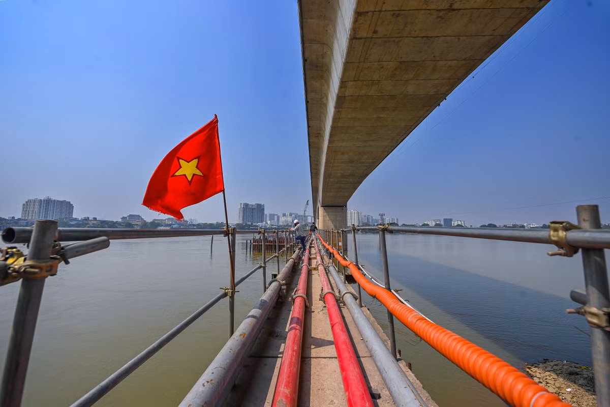 Một cây cầu tạm được thi công để đưa công nhân và vật liệu ra thi công ở giữa sông Hồng. Trước đó, nhà thầu phải thuê một cơ quan phụ trách phân luồng tàu bè, đảm bảo an toàn giao thông đường thủy qua khu vực.