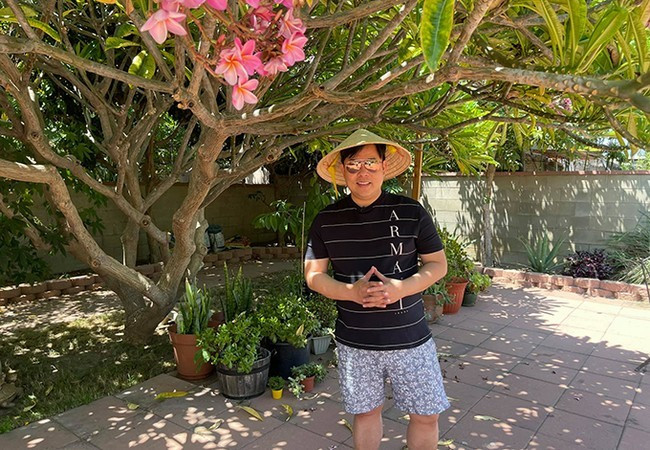 Quang Lê đeo kính đen, đội nón lá ra làm vườn ở Mỹ. Nam ca sĩ vừa tiêm xong vắc-xin phòng Covid-19.