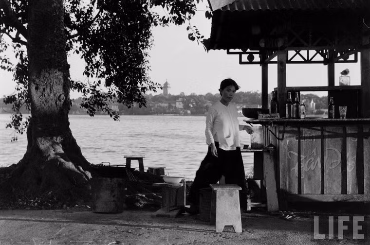 Quầy giải khát trên đường Cổ Ngư (nay là đường Thanh Niên) với hồ Trúc Bạch và tháp chuông nhà thờ Cửa Bắc ở hậu cảnh.